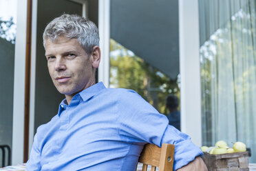 Portrait of mature man with grey hair sitting on terrace wearing blue shirt - TCF05643