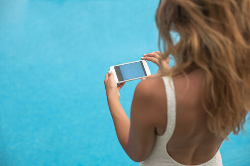 Junge Frau von hinten macht ein Foto vom Wasser im Schwimmbad mit einem Handy - ACPF00282