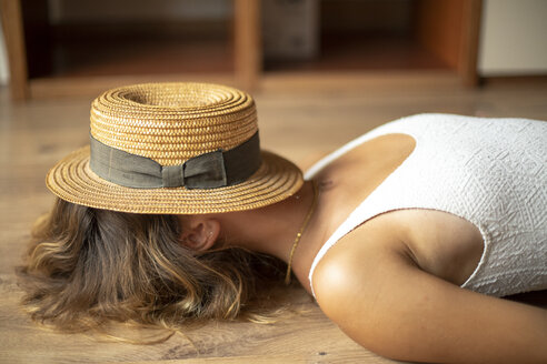 Eine unerkennbare junge Frau liegt mit einem Strohhut auf dem Kopf auf dem Boden - ACPF00288
