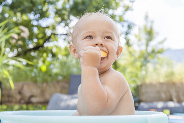 Junge sitzt in Babybadewanne und isst Obst - TCF05670