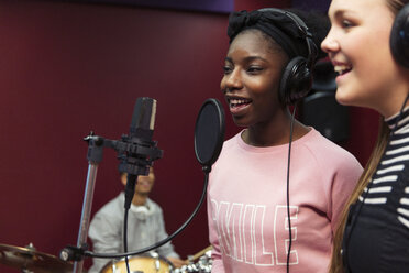 Teenage musicians recording music, singing in sound booth - CAIF21560