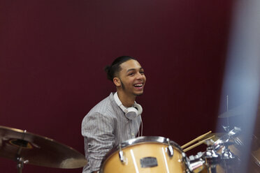 Happy teenage boy musician playing drums in sound booth - CAIF21569