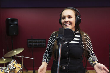 Confident teenage girl recording music, singing in sound booth - CAIF21570