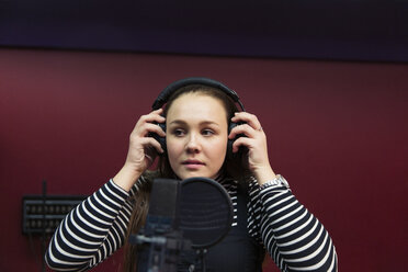 Teenage girl musician recording music, singing in sound booth - CAIF21576