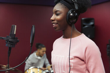 Smiling teenage girl musician recording music, singing in sound booth - CAIF21579