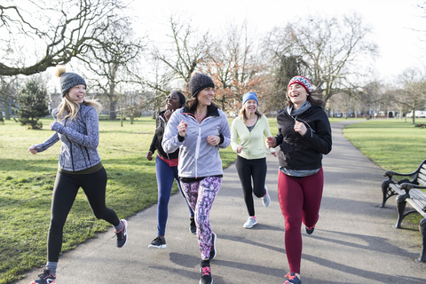 Lächelnde Läuferinnen laufen im sonnigen Park, lizenzfreies Stockfoto