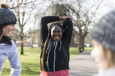 Lächelnde Läuferin beim Stretching im sonnigen Park - CAIF21590