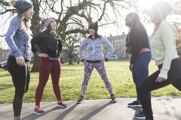 Female runners stretching and talking in sunny park - CAIF21592