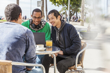 Männliche Freunde benutzen Laptop in einem sonnigen Straßencafé - CAIF21611