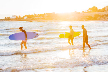 Male surfers carrying surfboards into ocean on sunny beach - CAIF21614