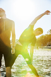 Männlicher Surfer streckt sich am sonnigen Strand - CAIF21617