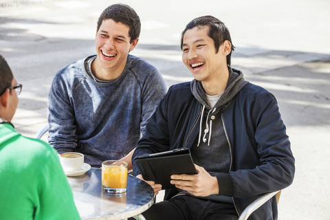 Männliche Freunde mit digitalem Tablet lachen in einem Straßencafé, lizenzfreies Stockfoto