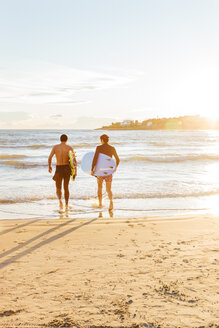 Männliche Surfer tragen an einem sonnigen Strand Surfbretter ins Meer - CAIF21623