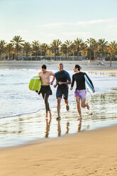 Enthusiastic male surfers running with surfboards on ocean beach - CAIF21631