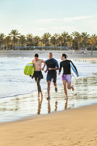 Begeisterte männliche Surfer laufen mit Surfbrettern am Strand - CAIF21631