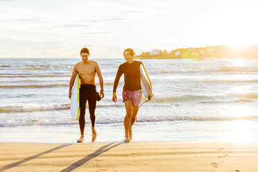 Male surfers carrying surfboards on sunny ocean beach - CAIF21640