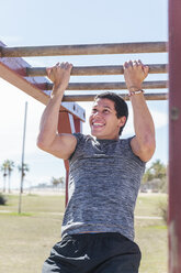 Determined man doing pull-ups on monkey bars - CAIF21643