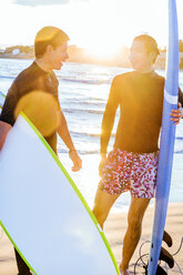 Männliche Surfer mit Surfbrettern unterhalten sich am sonnigen Strand - CAIF21644