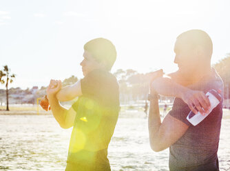 Männliche Läufer strecken die Arme am sonnigen Strand - CAIF21647