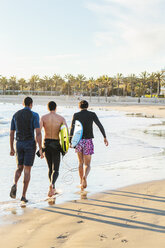 Männliche Surfer gehen mit Surfbrettern an einem sonnigen Strand spazieren - CAIF21648