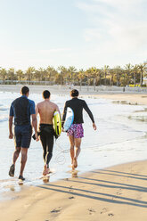 Male surfers walking with surfboards on sunny ocean beach - CAIF21648