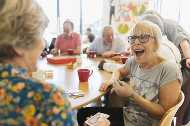 Glückliche ältere Frau spielt Karten mit einem Freund im Gemeindezentrum - CAIF21650