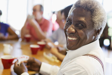 Porträt glücklicher älterer Mann, der mit Freunden im Gemeindezentrum Karten spielt - CAIF21655
