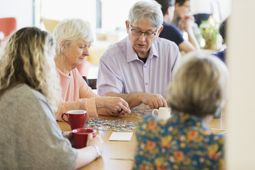 Ältere Freunde setzen ein Puzzle zusammen und trinken Tee am Tisch im Gemeindezentrum - CAIF21662