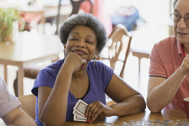 Confident, happy senior woman playing cards with friends in community center - CAIF21663