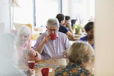 Senior friends playing games and drinking tea at table in community center - CAIF21664