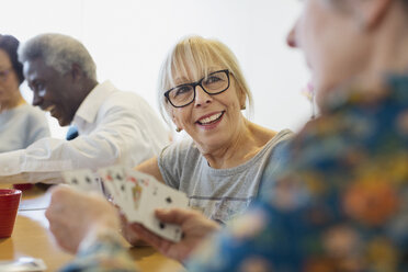 Lächelnde ältere Frau spielt Karten mit einem Freund im Gemeindezentrum - CAIF21668