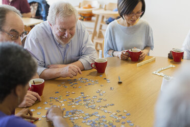 Ältere Freunde setzen ein Puzzle zusammen und trinken Tee am Tisch im Gemeindezentrum - CAIF21670