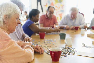 Ältere Frau setzt mit Freunden an einem Tisch im Gemeindezentrum ein Puzzle zusammen - CAIF21671