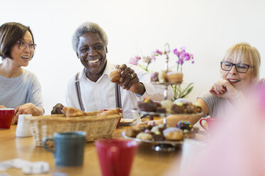 Happy senior friends enjoying afternoon tea desserts in community center - CAIF21677