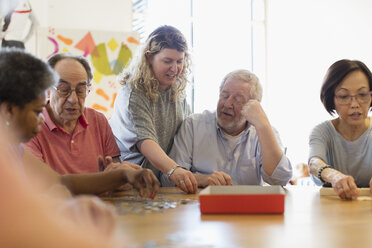 Freiwillige Helferin hilft einem älteren Mann beim Zusammensetzen eines Puzzles am Tisch im Gemeindezentrum - CAIF21679
