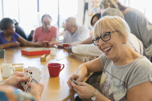 Happy senior woman playing cards with friend at table in community center - CAIF21682
