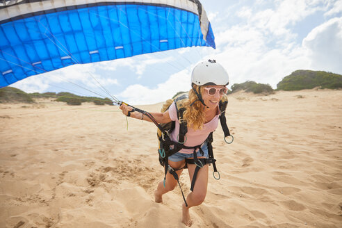 Lächelnde Gleitschirmfliegerin mit Fallschirm am Strand - CAIF21694