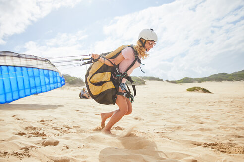 Gleitschirmfliegerin läuft mit Fallschirm am sonnigen Strand - CAIF21703