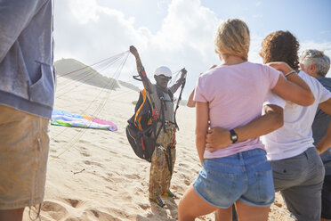 Schüler beobachten männlichen Paragliding-Lehrer mit Ausrüstung am sonnigen Strand - CAIF21710