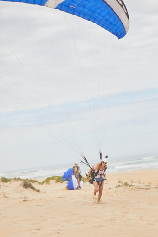 Weiblicher Gleitschirmflieger mit Fallschirm am Meeresstrand, lizenzfreies Stockfoto
