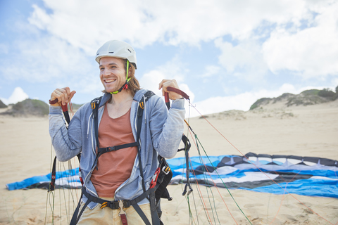 Lächelnder, selbstbewusster Gleitschirmflieger mit Fallschirm am Strand, lizenzfreies Stockfoto