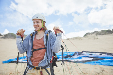 Lächelnder, selbstbewusster Gleitschirmflieger mit Fallschirm am Strand - CAIF21717