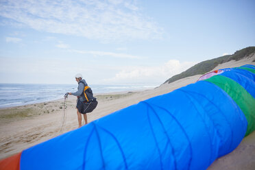 Männlicher Gleitschirmflieger mit Fallschirm am Meeresstrand - CAIF21724