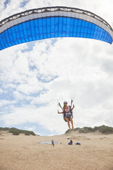 Gleitschirmfliegerin mit Fallschirm, die am Strand abhebt - CAIF21725