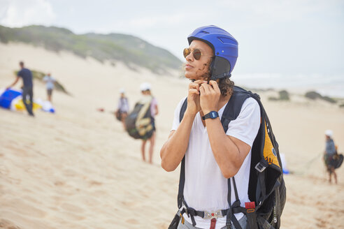 Männlicher Gleitschirmflieger befestigt seinen Helm am Strand - CAIF21726