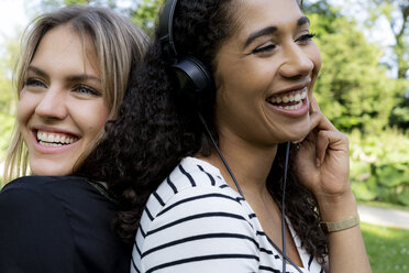 Two girlfriends in a park listening music, laughing, having fun - HHLMF00318