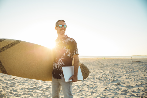 Mann am Strand mit Surfbrett und Laptop, lizenzfreies Stockfoto