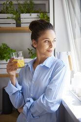 Young woman drinking orange juice in her kitchen - ABIF00899