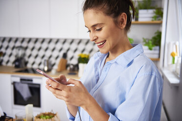 Young woman using smartphone in the kitchen - ABIF00904