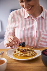 Junge Frau, die frische Pfannkuchen mit Beeren garniert - ABIF00930